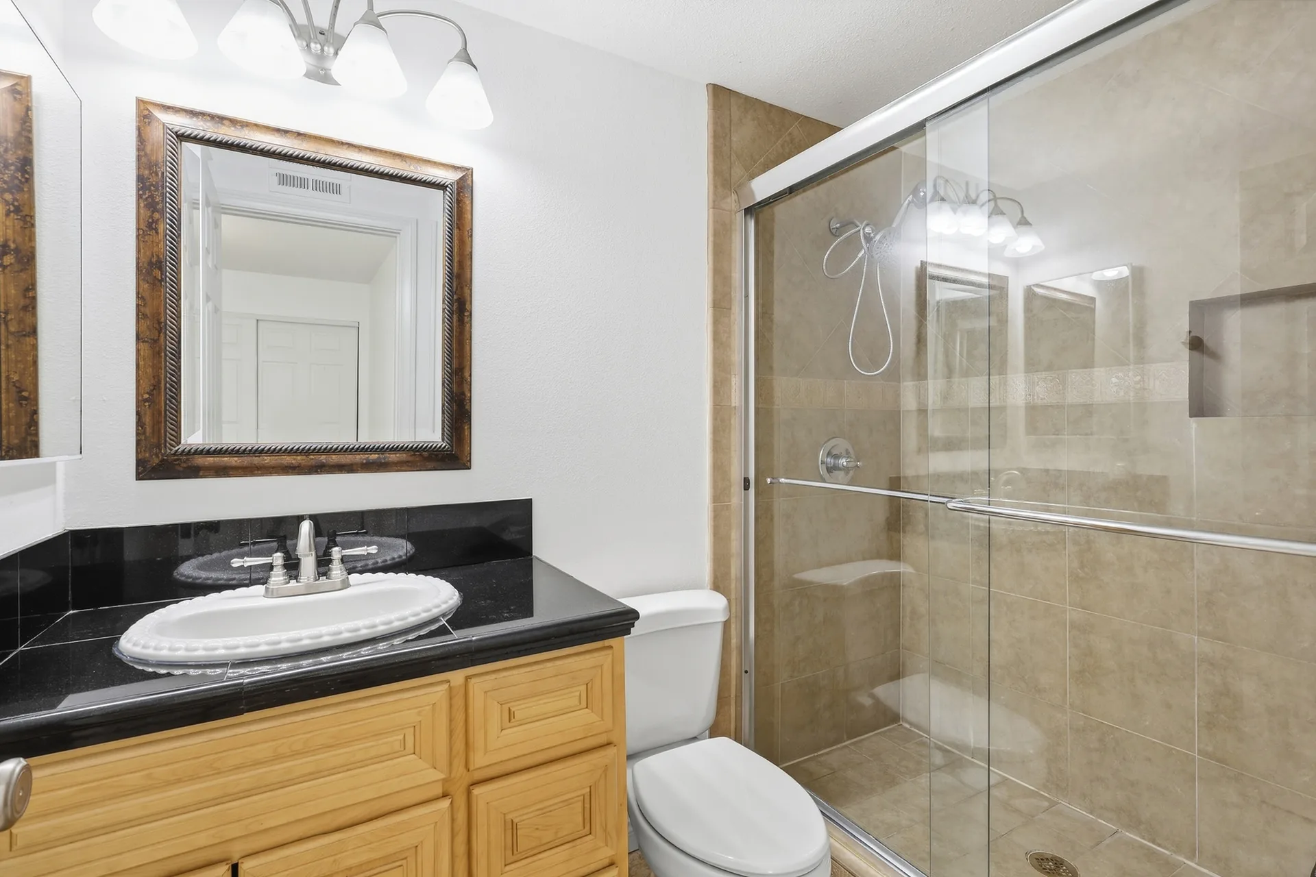 Bathroom at 8 Silverwood with an oak vanity, black granite counter, and glass-door shower