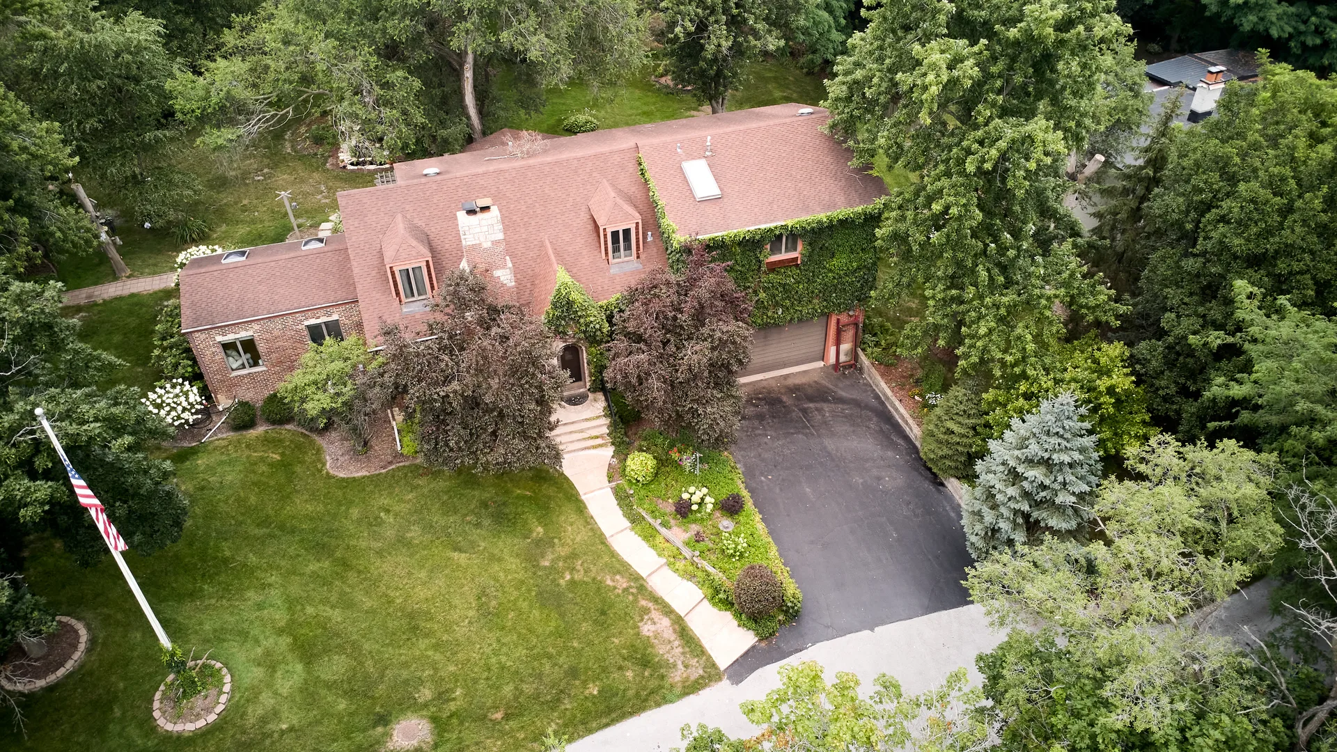 Drone view of the house, front lawn, and surrounding trees