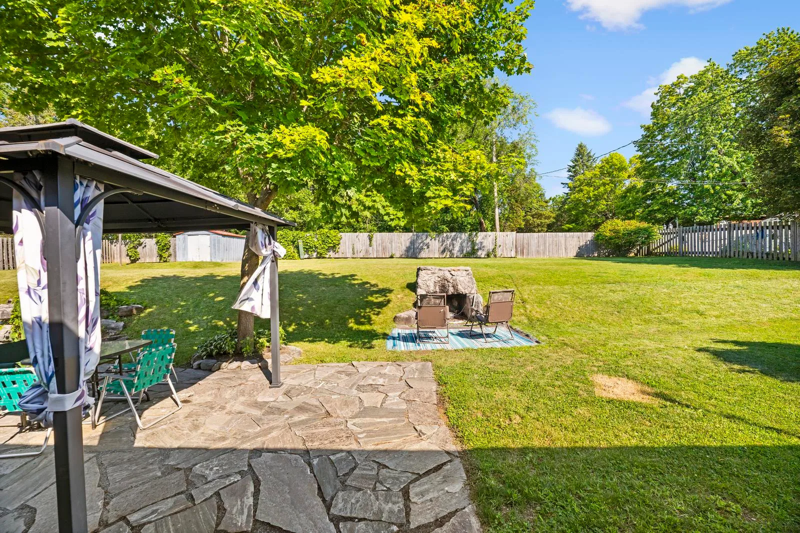 View from stone patio looking out at large open lawn with wooden privacy fence