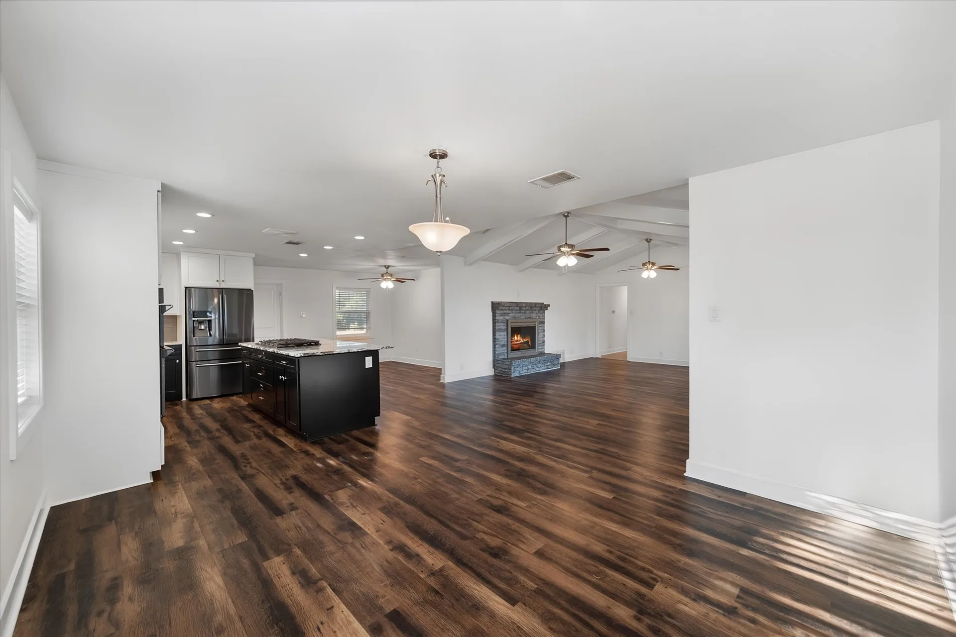 Wide-angle living and kitchen view with stone-faced fireplace and dark floors