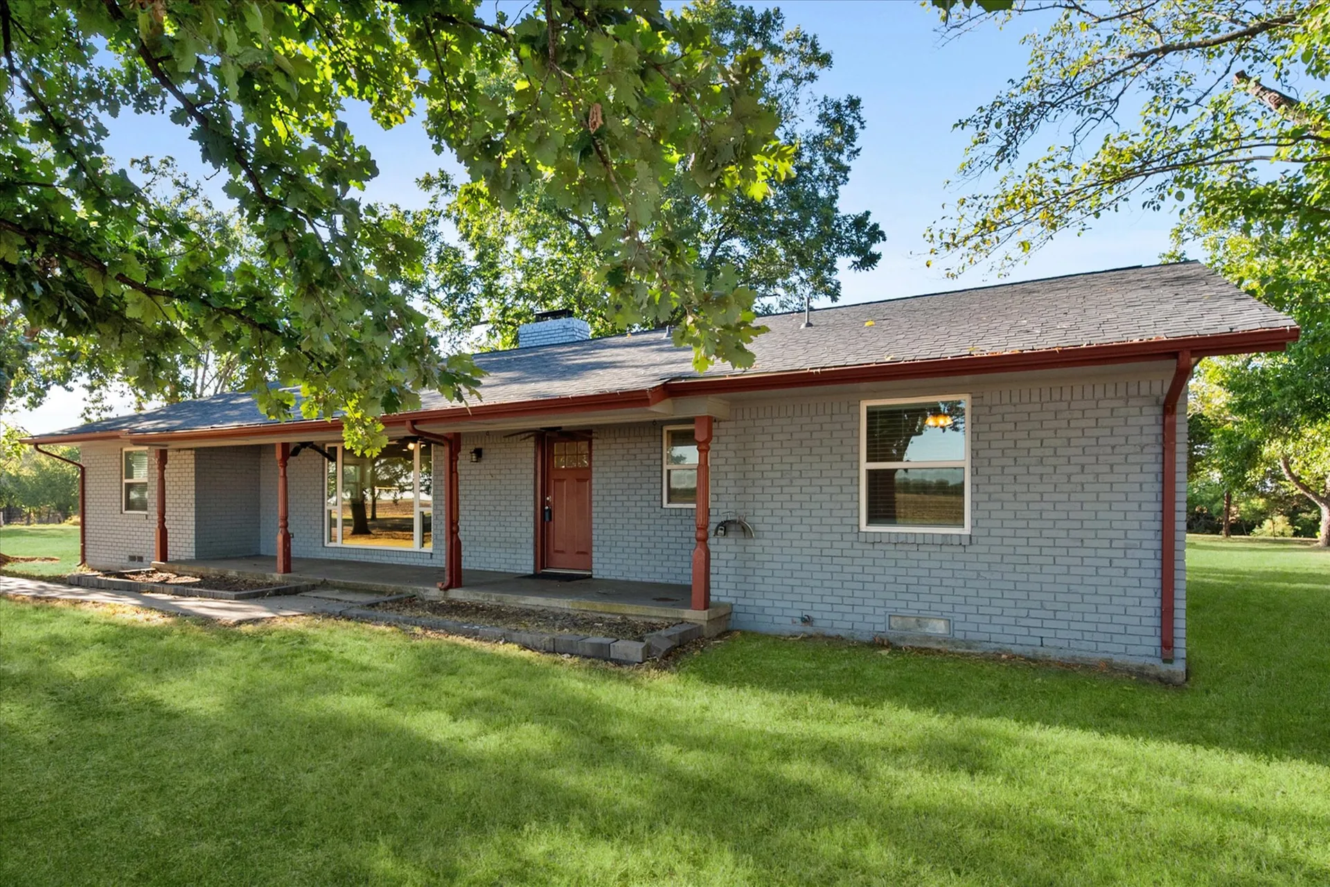 Front exterior of the painted-brick ranch home under partial oak shade